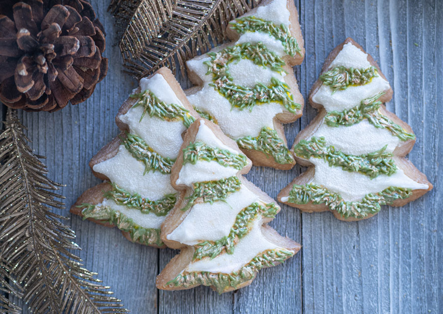 Christmas tree-shaped frosted cookies with green icing on a wooden surface