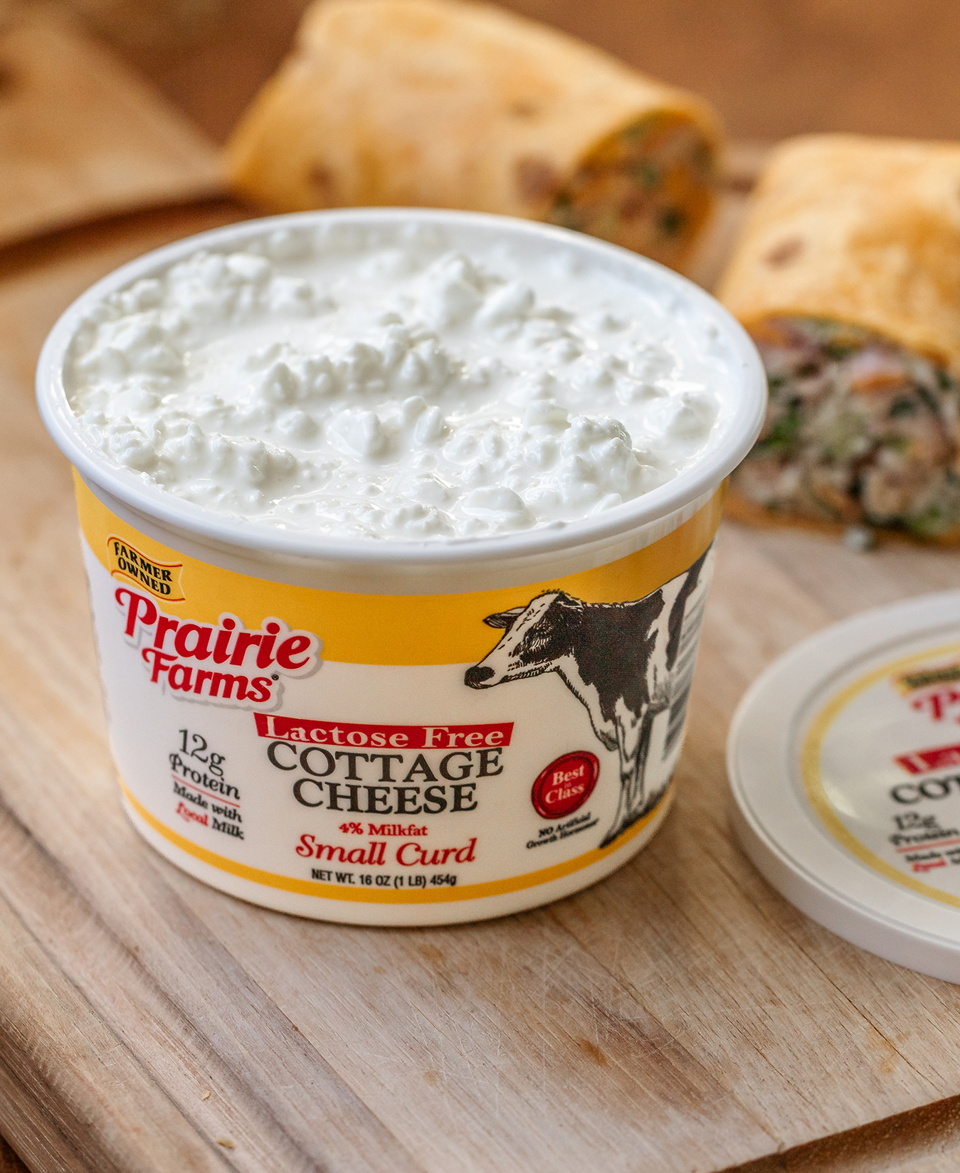 Prairie Farms Lactose Free Small Curd Cottage Cheese container on a wooden board with wraps in the background
