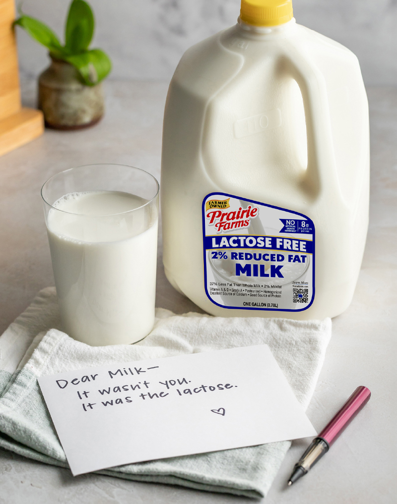 Prairie Farms Lactose Free 2% Reduced Fat Milk gallon beside a glass of milk and a handwritten note reading, “Dear Milk—It wasn’t you. It was the lactose.”