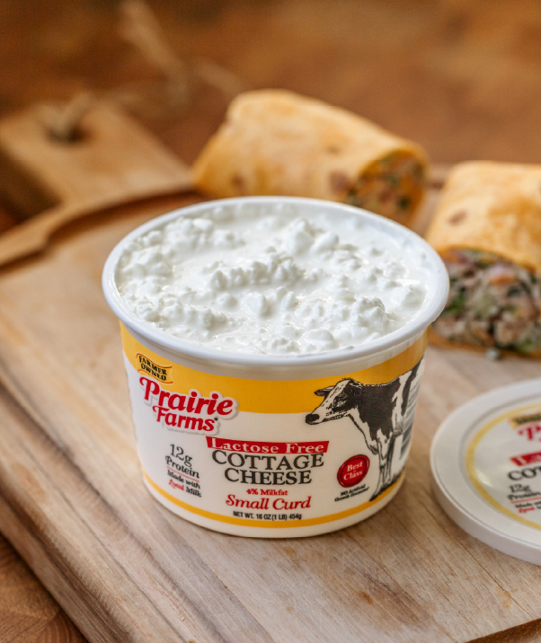 Prairie Farms Lactose Free Small Curd Cottage Cheese container on a wooden board with wraps in the background