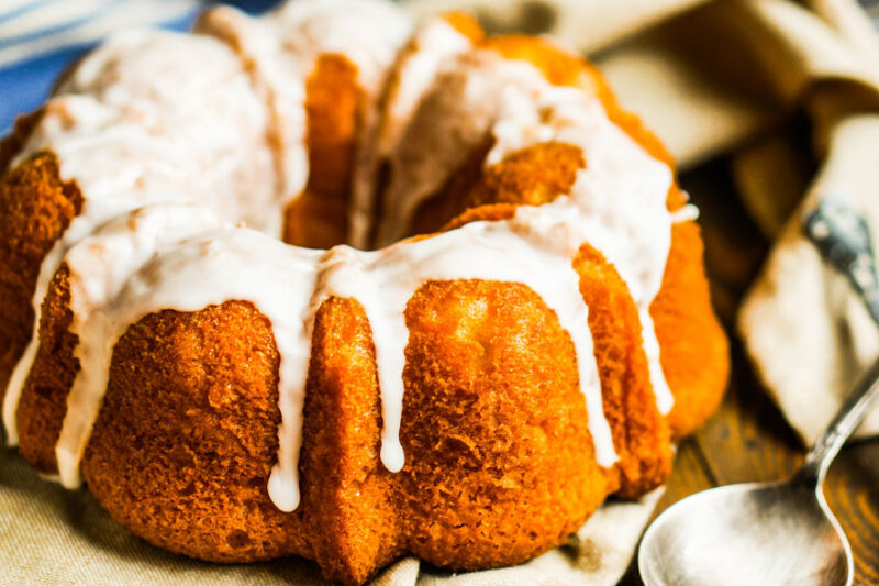 Glazed Bundt cake on a cloth, with a spoon beside it.