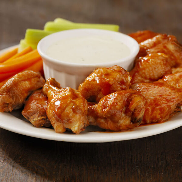 Plate of Buffalo chicken wings with a ramekin of dipping sauce in the center.