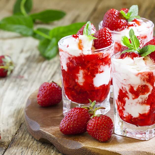 Three glasses of strawberry and whipped cream dessert topped with fresh strawberries and mint