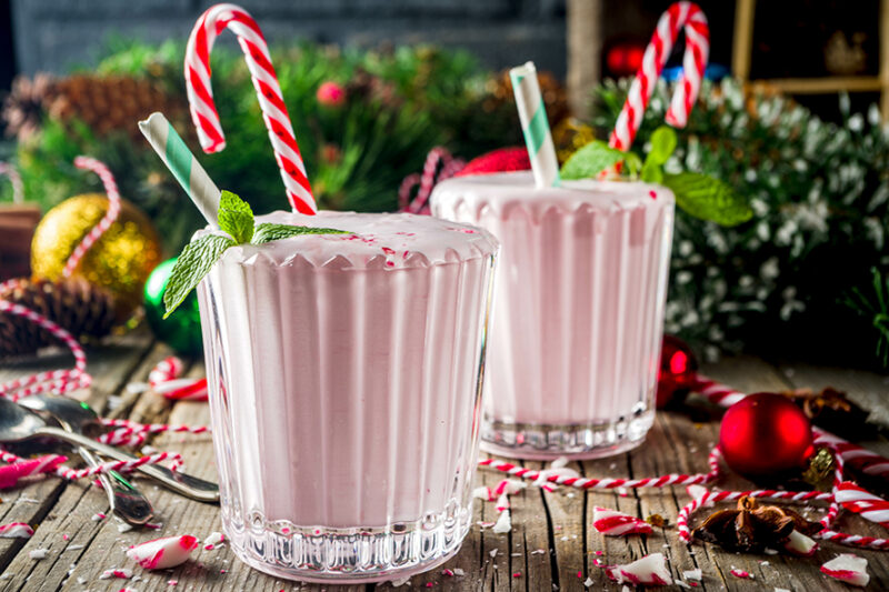 Two pink milkshakes in glasses with peppermint candy canes and mint on a wooden table