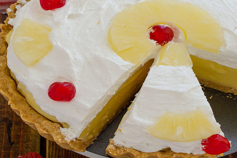 Pineapple pie topped with whipped cream, pineapple slices, and cherries, with a slice cut out