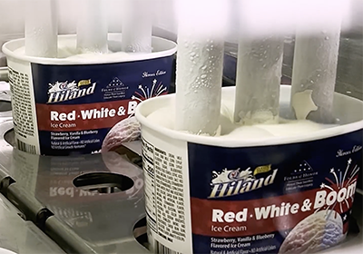 Hiland Red, White & Boom Ice Cream containers on a production line being filled from vertical nozzles dispensing ice cream