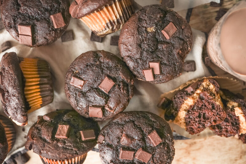 Chocolate peanut butter muffins topped with chocolate chunks, with one muffin cut open to reveal a creamy peanut butter filling.