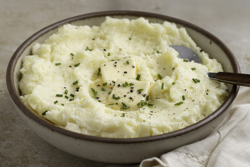 Creamy mashed potatoes served in a rustic bowl, topped with melting butter, chopped chives, and freshly ground black pepper.