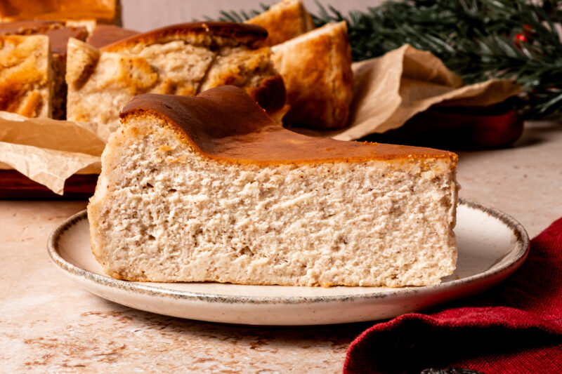 A thick slice of gingerbread Basque cheesecake with a golden brown top and creamy, spiced interior on a ceramic plate.