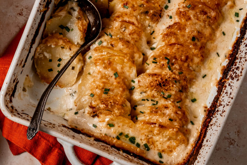 Golden brown sour cream and chive potato gratin baked in a white casserole dish.